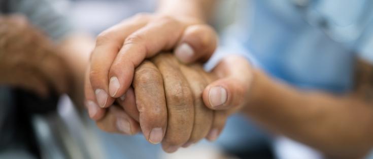 Elder patient holding a nurse's hand with care.