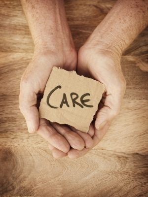 Care written on small piece of cardboard held in hands over wood background.