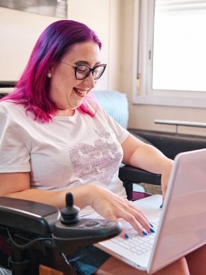 Adult woman with disabilites in a wheelchair shopping at home with laptop.